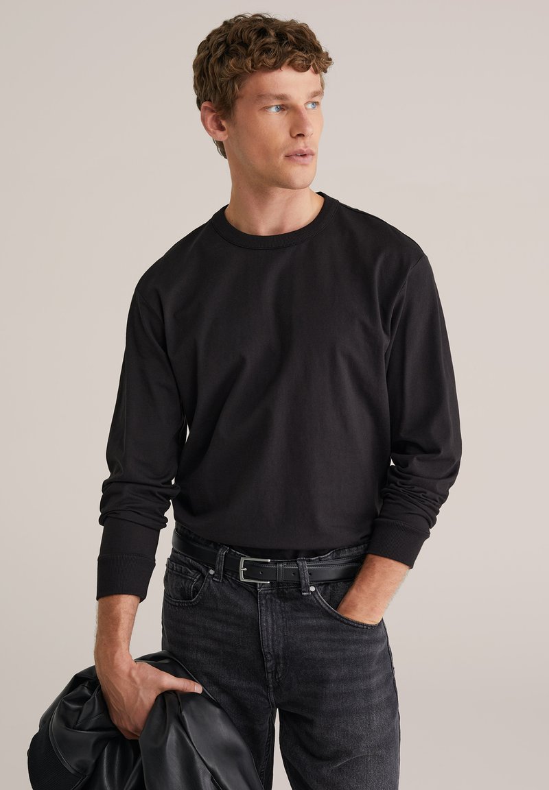 Juoda ilgomis rankovėmis medvilninė palaidinė su apvalia iškirpte ir ribinėmis rankogaliais, derinama su tamsiomis džinsais ir laikoma juoda odine striuke.