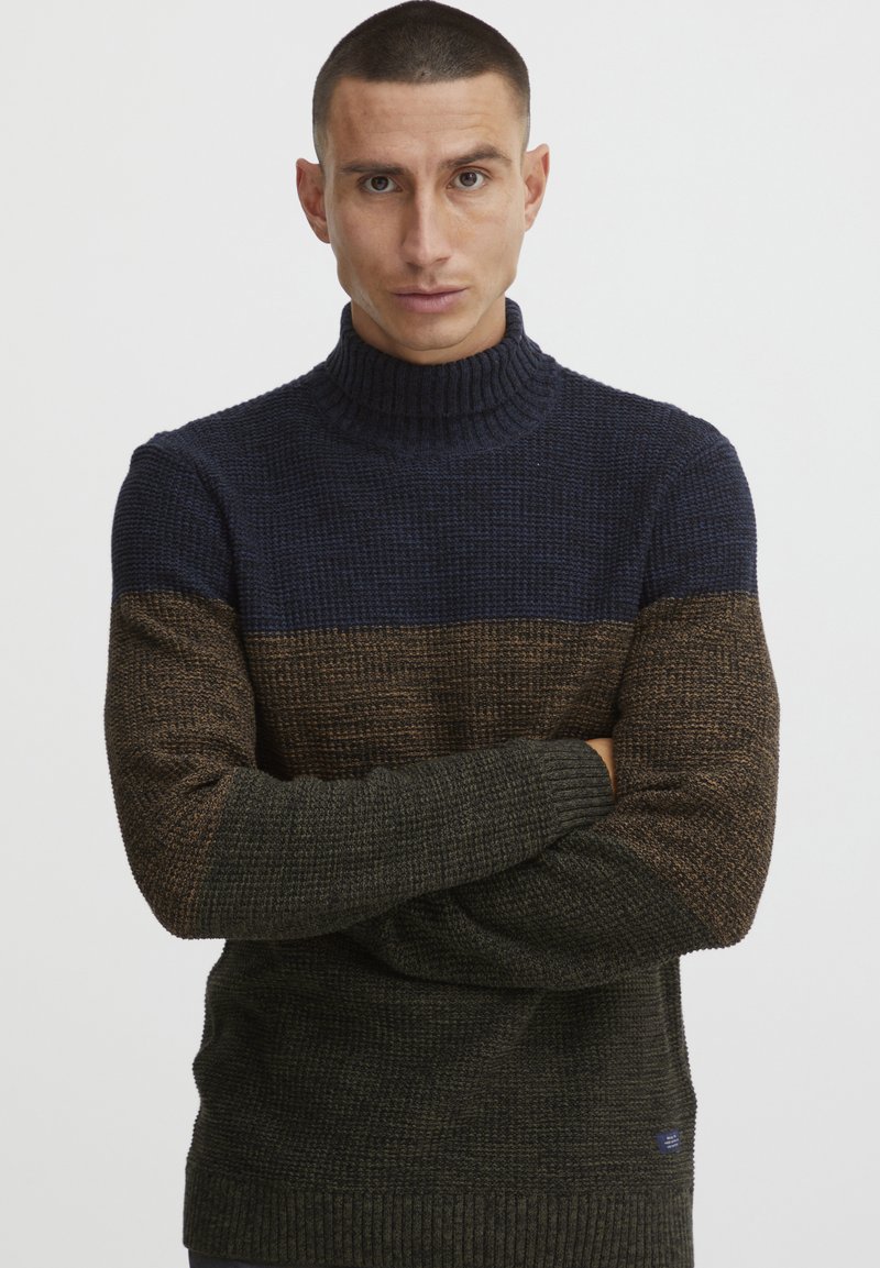 Maglione a collo alto lavorato a maglia in blu scuro, marrone e verde. Texturizzato, con polsini e orlo a coste. Presenta un piccolo logo sul lato.