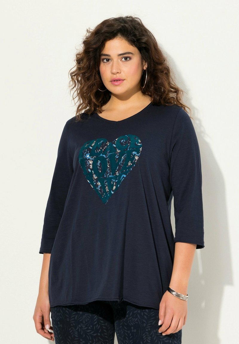 Navy-blaues langärmliges T-Shirt mit einem türkisfarbenen Herzdesign, das Blumenmuster aufweist. Glatte Textur, lockere Passform und runder Ausschnitt.