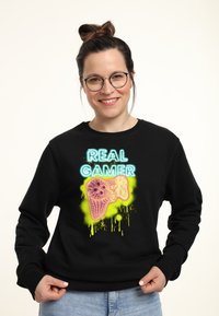 Felpa nera con design al neon che leggono "REAL GAMER" accompagnati da una grafica di un controller di gioco. Tessuto morbido con vestibilità comoda.