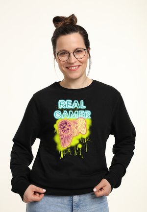Schwarzer Hoodie mit neonfarbenen Designs, die "ECHTER SPIELER" und ein Grafik eines Gamecontrollers zeigen. Weicher Stoff mit lässiger Passform.