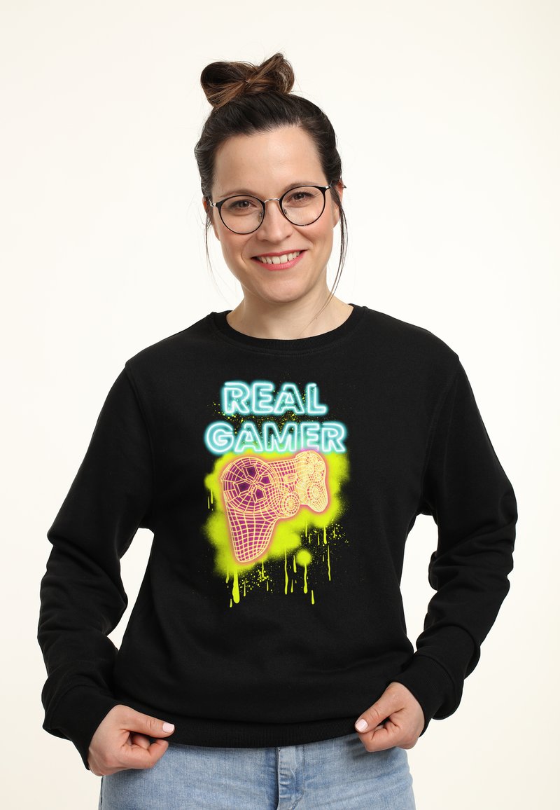 Felpa nera con design al neon che leggono "REAL GAMER" accompagnati da una grafica di un controller di gioco. Tessuto morbido con vestibilità comoda.