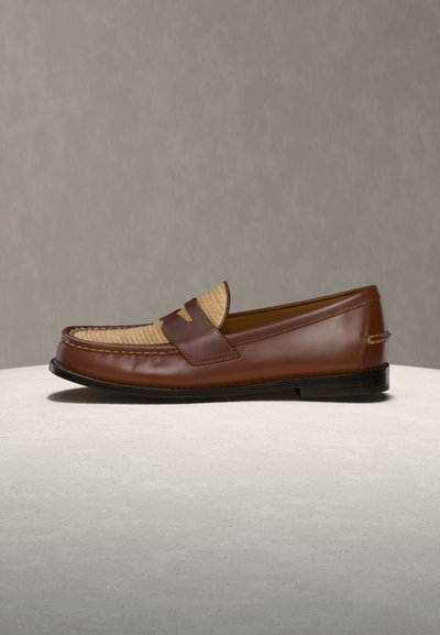 Vyrų rudos spalvos odiniai bateliai su megzto smėlio spalvos dekoru viršuje, juodu padu ir slip-on dizainu, padėti ant šviesios spalvos paviršiaus.