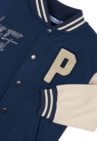 Giacca varsity blu navy con colletto e polsini a coste grigi e crema a strisce, caratterizzata da una toppa "P" beige testurizzata e bottoni a pressione.