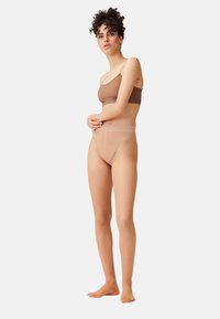 BH und hochgeschnittene Unterwäsche aus einem glatten, dehnbaren, nudefarbenen Stoff. Nahtloses Design mit dünnen Trägern und einem breiten elastischen Bund.