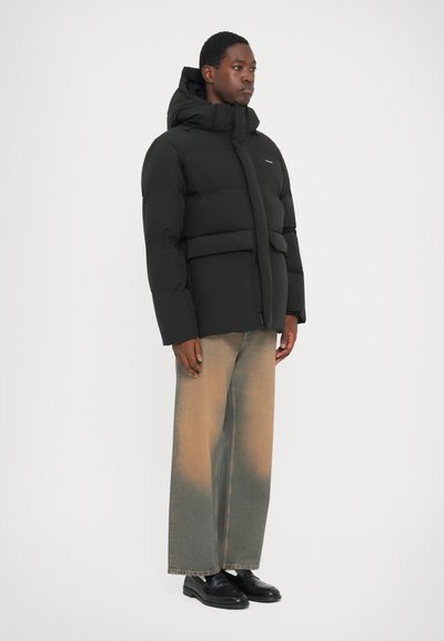 Black puffer jacket with a high collar, front toggles, and horizontal seams. Paired with light faded wide-leg jeans and black shoes.