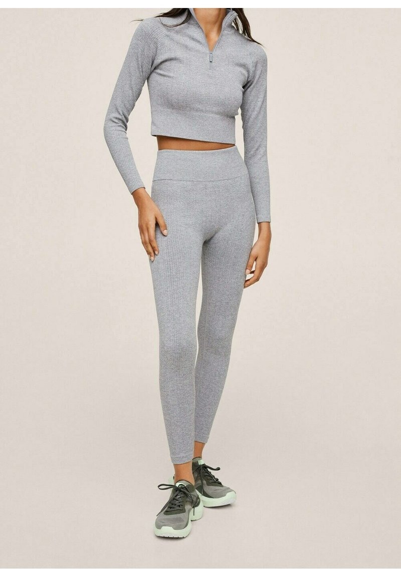 Haut court à manches longues côtelé gris avec un col zip et leggings taille haute. Associé à des chaussures de sport noires et vert clair.