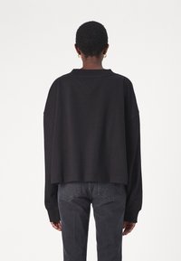 Black cropped sweatshirt with long sleeves, ribbed collar, and stitched detailing at the shoulder. Worn with dark gray jeans.