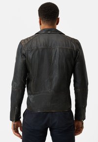Schwarze Leder-Motorradjacke mit tailliertem Design, gesteppte Schultereinsätze und Reißverschlussmanschetten. Glatte Textur mit sichtbaren Nähten.
