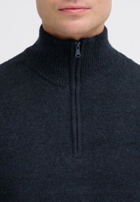 Donkergrijze zip-up trui met een hoge ribbelkraag, gemaakt van een gestructureerd breimateriaal, met een zachte rits bij de hals.