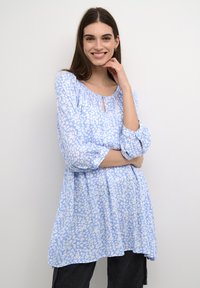Jasnoniebieska bluzka z białym wzorem w kwiaty, okrągły dekolt i detal w kształcie dziurki. Posiada rękawy 3/4 w stylu bufiastego i luźny krój.