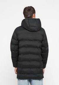 Musta vuorattu takki hupulla, jossa on tikattu muotoilu ja joustavat hihansuut, pituudeltaan keskivarteen asti. Pehmeä, sileä kankaan pinta.