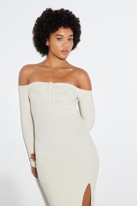 Robe crème à côtes, dénudée sur les épaules, avec des manches longues et une fente haute sur la cuisse. Détail de lien ajustable au niveau de la poitrine. Texture lisse et douce.