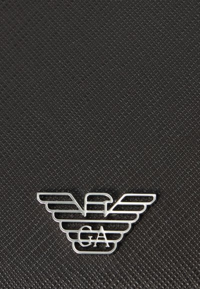 Srebrne skrzydlate logo z literami „GA” na tle teksturowanym czarnym, z równoległymi liniami i wypukłym wzorem.