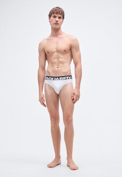 Calzoncillos blancos con una cinturilla negra que dice "SQUARED?". La tela parece suave; el diseño es minimalista, con un corte clásico.