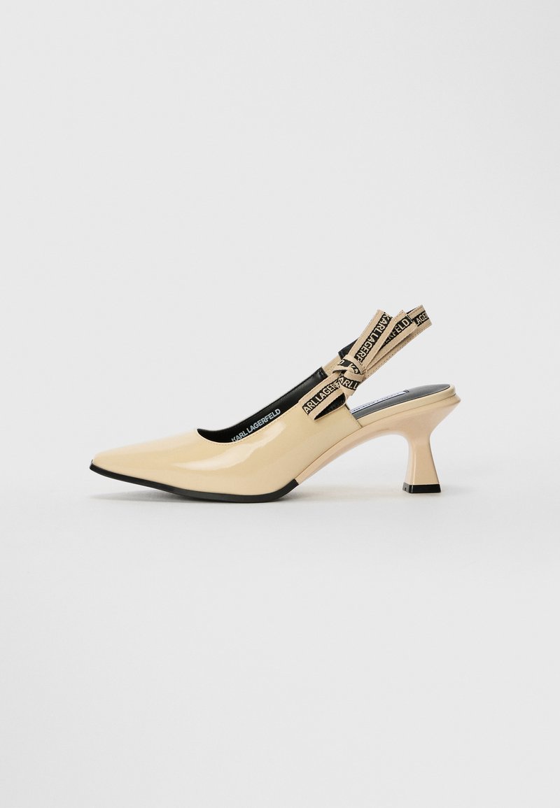 Beige lakked skinnesko med slingback, spiss tå, dekorert stropp med logo, og en liten blokkhelt med svart base.