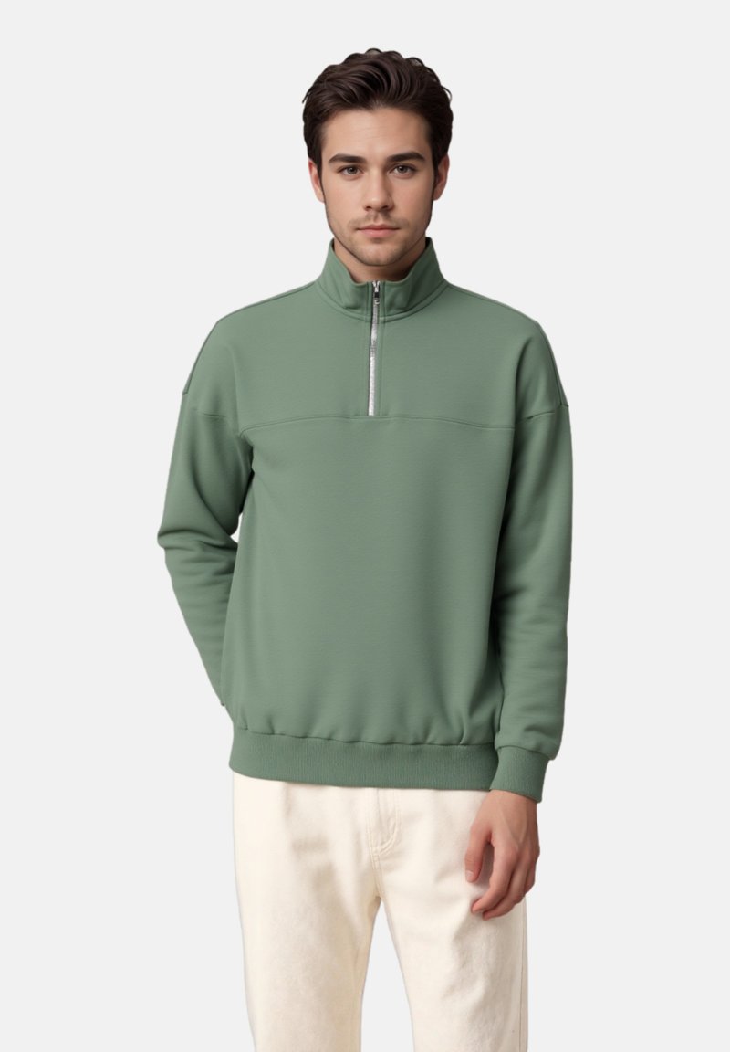 Pull-over vert à demi-fermeture éclair en tissu doux, doté d'un ourlet et de poignets côtelés, avec un accent de fermeture éclair lisse sur le col.
