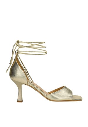 Gold metallic heeled sandal with an open toe, a slip-on design, and thin ankle straps. Features a slender high heel and smooth texture.