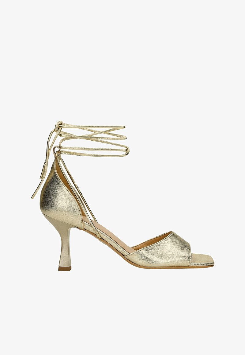 Złote metaliczne sandały na obcasie z odkrytymi palcami, slip-on, z cienkimi paskami na kostkę. Posiadają smukły wysoki obcas i gładką fakturę.