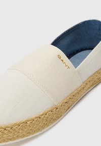 White canvas espadrille with jute sole, featuring a gold logo accent on the upper band and a soft denim lining inside.