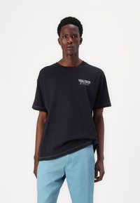 Black cotton t-shirt with short sleeves, a loose fit, featuring white "VOLCOM STORE" graphic on the chest and contrasting stitching.