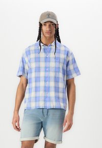 Short-sleeve, button-up shirt in light plaid with blue, white, and pink hues; soft texture; paired with light blue denim shorts.
