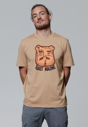 Beige Baumwoll-T-Shirt mit einem Grafikdesign von einer gerösteten Brotscheibe mit Gesichtszügen und dem Text "TOAST MALONE" in dunkler Schrift.