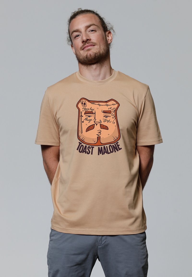 Beige katoenen t-shirt met een afbeelding van een geroosterde sneetje brood met gezichtskenmerken en de tekst "TOAST MALONE" in donkere letters.