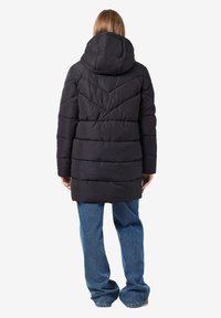 Doudoune noire avec capuche, présentant un motif matelassé en chevrons et un design légèrement cintré, associée à un pantalon en denim bleu ample.
