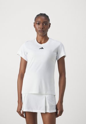 Hvit atletisk topp med korte ermer og rund hals, med en liten svart logo på brystet, parret med en matchende hvit plissekjole.