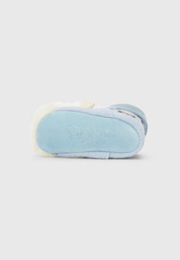 Papuci de culoare albastru deschis, cu exterior din fleece moale, margine contrastantă din blană crem și talpă texturată de culoare albastră. Prezintă detalii cusute ale mărcii.