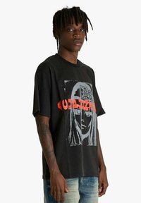 T-shirt nera in cotone con maniche corte, con stampa grafica di un volto e testo stilizzato in rosso. Vestibilità comoda e scollo rotondo.