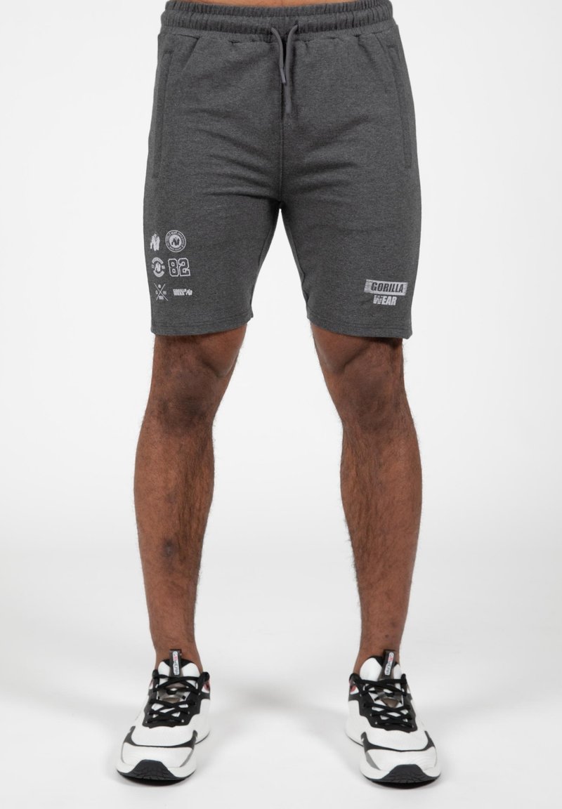 Grijze sportshorts met een elastische tailleband, zakken en bedrukte graphics aan de linkerkant en op het rechterbeen. Gecombineerd met zwart-witte sneakers.