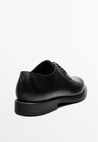 Black leather shoe with a smooth finish, rounded toe, and five-eyelet lacing. Features a slightly raised, textured rubber sole.
