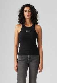 Črna rebrasta majica brez rokavov s krožnim izrezom in belim logotipom "LEVI'S" na prsih, v kombinaciji s sivo visokim pasom.