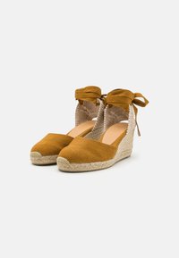 Hnědé plátěné wedge espadrilky s tkanou jutu podešví, stahovacími stužkami kolem kotníků a otevřenými stranami s polyesterovým designem pro prodyšnost.