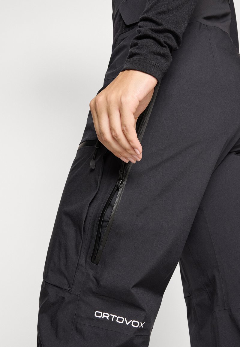 Schwarze Outdoor-Hosen mit einer Reißverschlusstasche an der Seite, aus strapazierfähigem Stoff mit glatter Textur. Das "ORTOVOX"-Logo ist sichtbar.