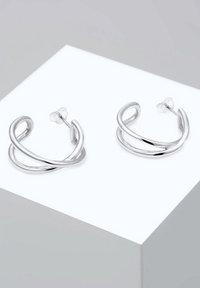Paire de boucles d’oreilles créoles torsadées en argent poli avec fermoirs à tige sur un bloc d’exposition blanc.
