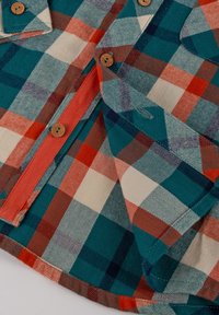 Camicia in flanella con un motivo a quadri multicolore in teal, rosso e crema; presenta bottoni in legno e accenti arancioni a contrasto.