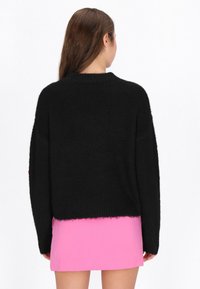 Schwarzer, plüschiger Strickpullover mit lockerer Passform und ribbeltem Saum, kombiniert mit einem rosa, figurbetonten Minirock. Keine sichtbaren Muster oder Akzente.