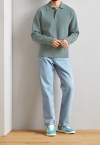 Polo à manches longues vert clair avec col, associé à un jean bleu clair à jambes droites et des baskets bleu sarcelle à rayures blanches.