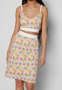 Kaksiosainen asu, joka koostuu lyhyestä toppista ja kynähameesta. Kangas on monivärinen ja siinä on geometrista kuviota pastelliväreissä.