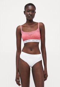 Roze čipkasti bralette s tankim trakama i bijelim rastezljivim gaćicama. Bralette ima brendiranu elastičnu traku. Glatka tekstura, ženstveni dizajn.