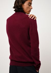 Maglione morbido in maglia bordeaux con collo alto, polsini e orlo a coste. Presenta un design aderente, texture visibile e linee pulite.