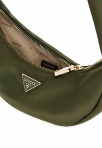 Sac en nylon vert olive avec une fermeture éclair dorée, présentant un logo triangular et une texture lisse et mate. Intérieur clair.
