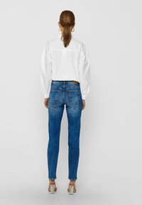 Vit långärmad skjorta i kombination med blå denimjeans. Jeansen har en urblekt finish, knappstängning och bakfickor. Silverfärgade klackskor avslutar looken.