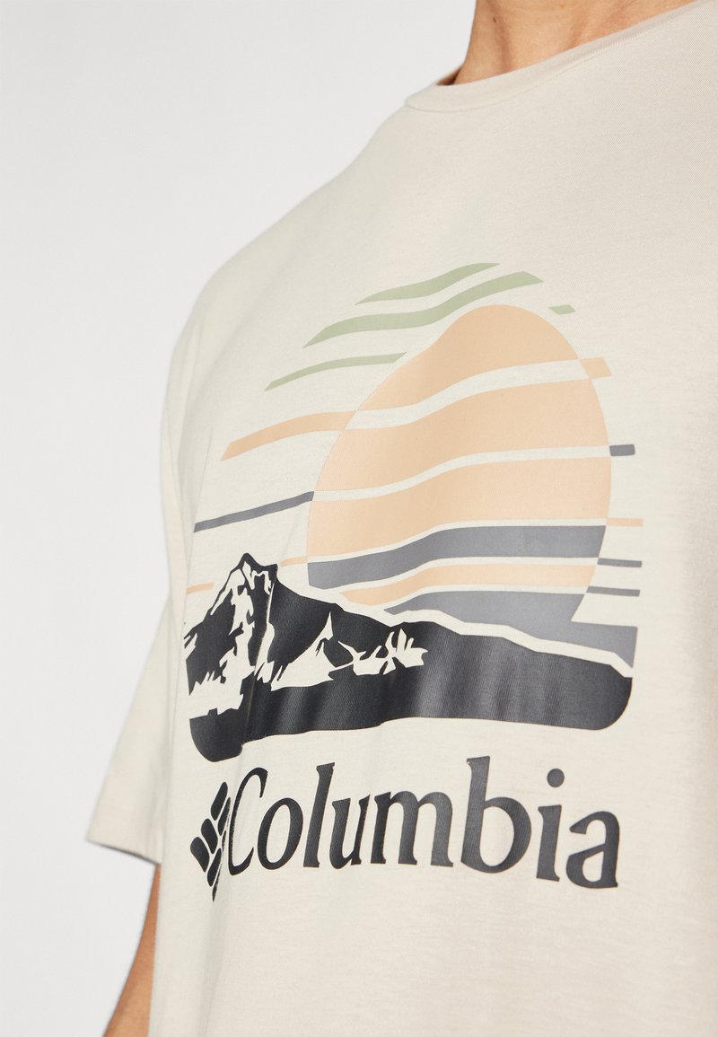 Maglietta color crema con una stampa grafica che raffigura montagne, un tramonto e linee orizzontali in colori pastello. Logo "Columbia" sotto il design.