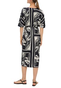 Robe à motifs noir et blanc avec des manches courtes, taille cintrée et coupe mi-longue ; portée avec des sandales plates noires. Texture du tissu lisse.