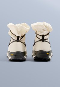 Wysokie buty z kremową cholewką ze ściąganym mankietem, czarnymi sznurowadłami i teksturowaną podeszwą Vibram zapewniającą przyczepność.