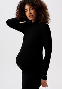 Schwarzes, geripptes Kleid mit langen Ärmeln und taillierter Silhouette, das die Körperform betont. Der Stoff wirkt dehnbar und weich.